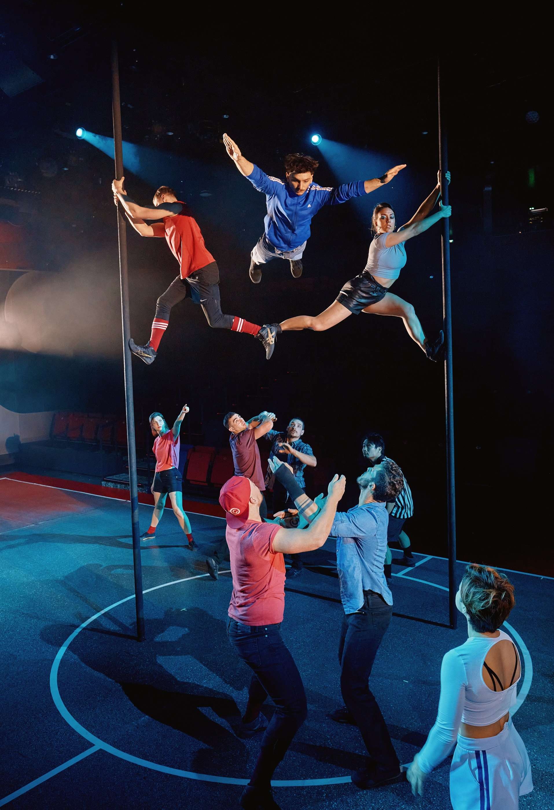 Deux équipes d'artistes, les bleus et les rouges s'affrontent en acrobaties. Certains sont sur des mâts métalliques. 